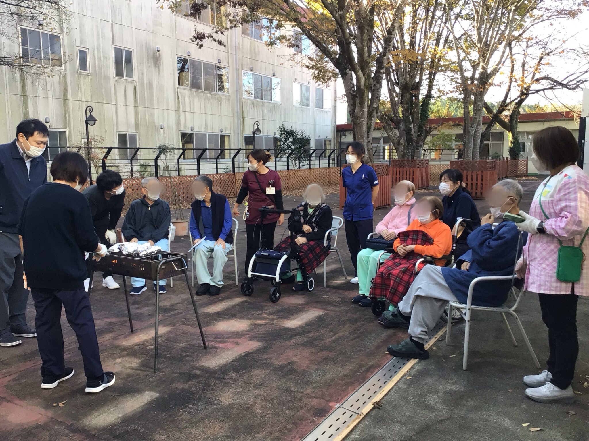 施設の庭園でスタッフと入居者が集合し、イベントや集団活動を行っている様子。